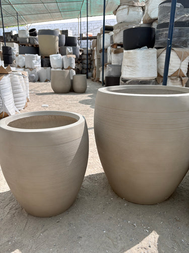 Fiber Pot Aura Beige Lifetime Warranty in UAE. Beige cylindrical concrete pots on a concrete surface with a blurred background