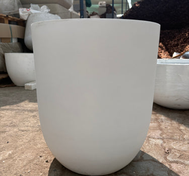 White Arco Fiber Pot with Matte Finish and Lifetime Warranty, UAE. Close-up of a white ceramic vase against a textured stone wall.